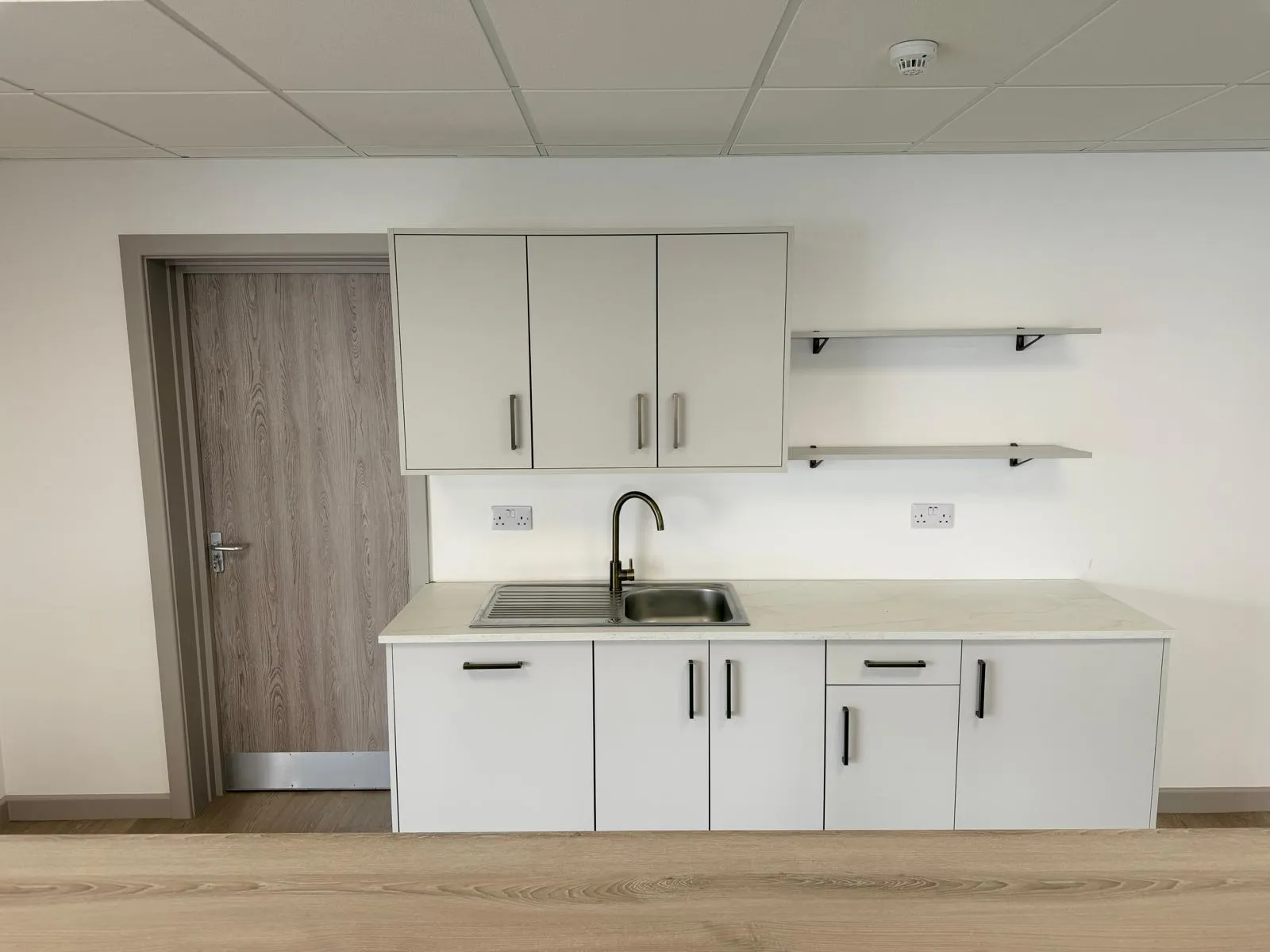 Kitchenette with white cabinetry, worktops, sink, and vinyl plank flooring at Boluda Towage