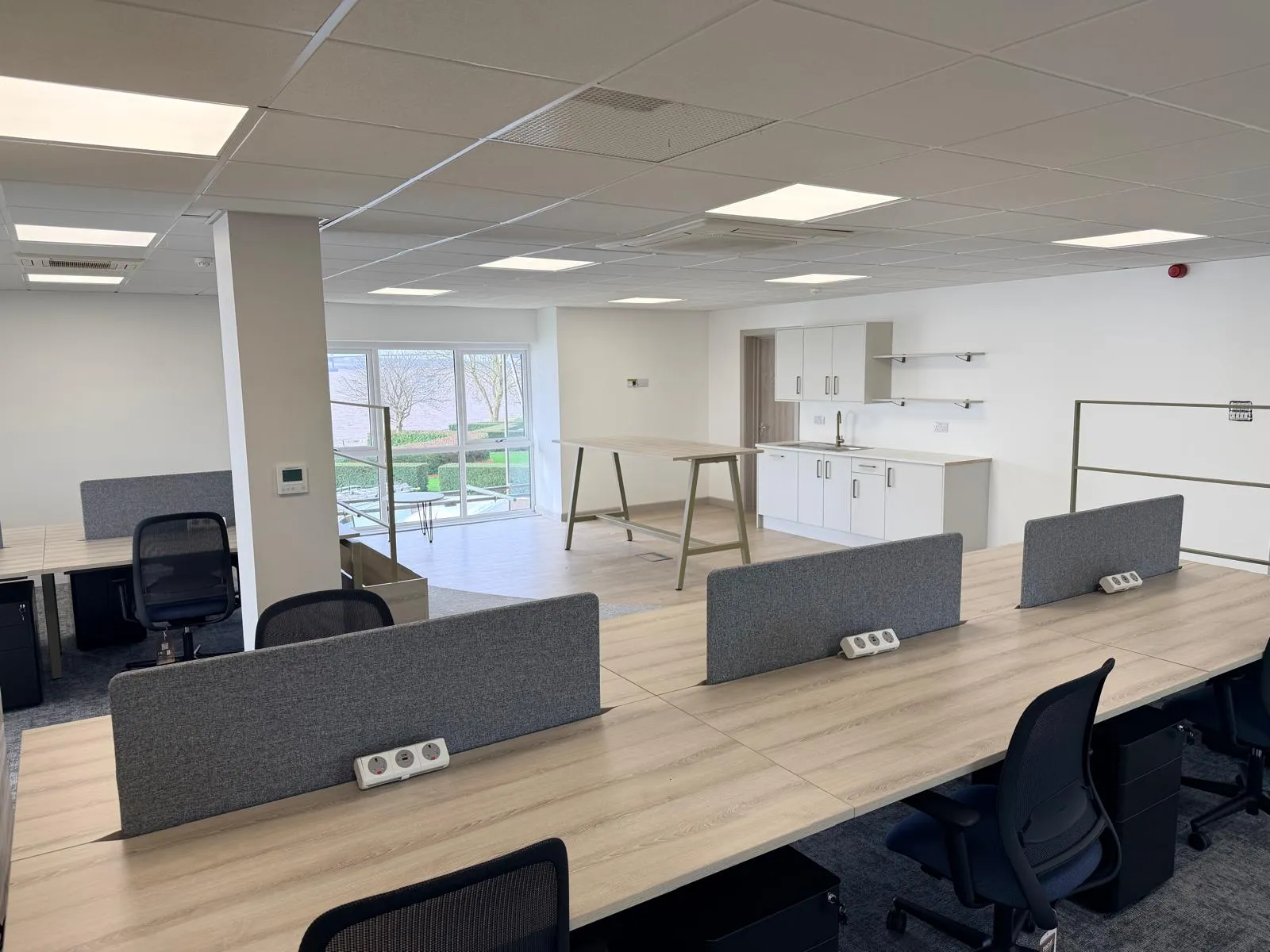 Open-plan workspace with bench desks, kitchen area, and standing height table at Boluda Towage