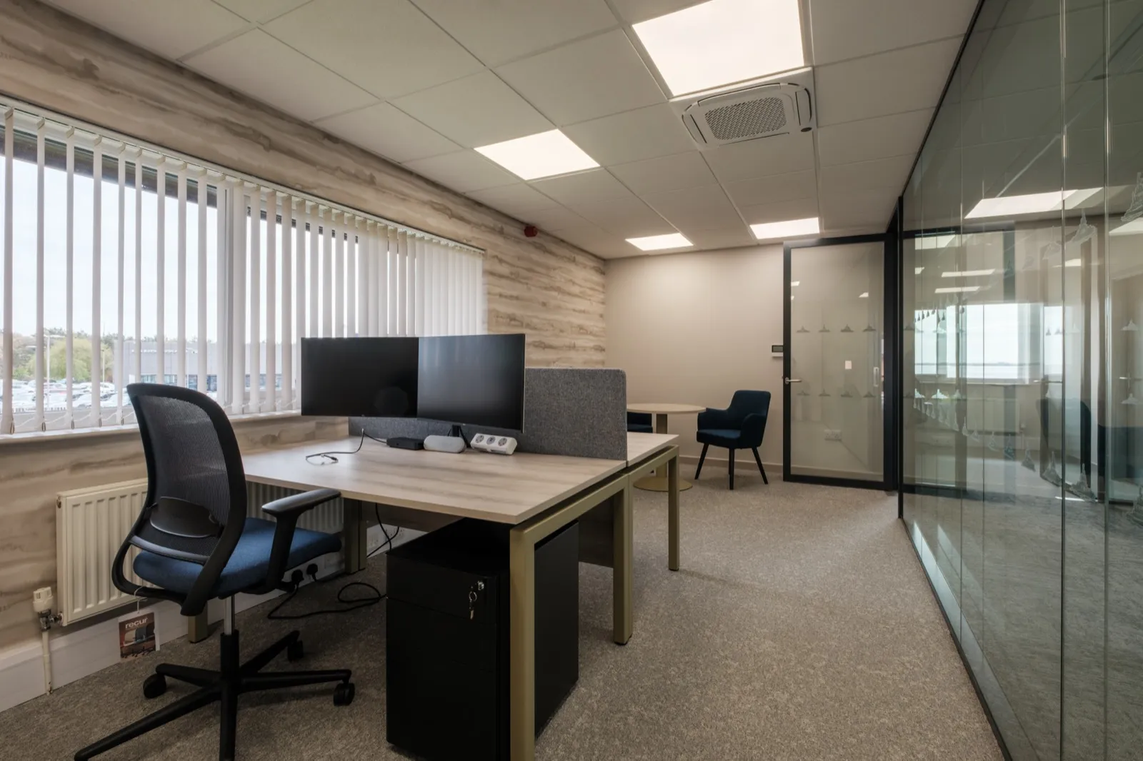 Private office with a sit-stand desk, blue tub chair and small round meeting table at Boluda Towage